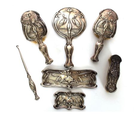 An Art Nouveau silver dressing table set comprising of three brushes, hand mirror, two trays, and a silver handled button hoo