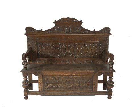 A LATE 19TH CENTURY STAINED AND CARVED OAK MONK'S BENCH, the arch raised back with foliate scrollwork above a lift top seat, 