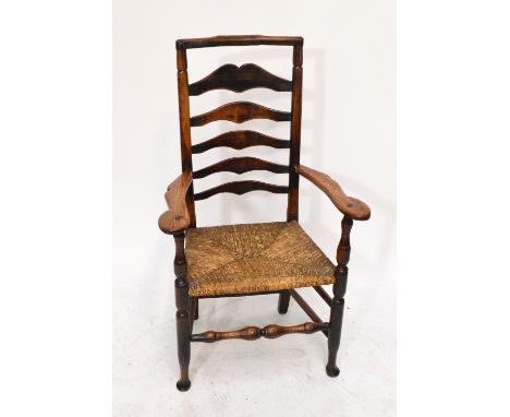 An early 19th century ash and elm country made high wavy ladder back elbow chair with shaped top rail, broad swept arms, rush