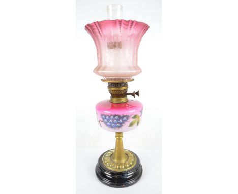 An early 20th century oil lamp with circular brass base, pink opaque glass reservoir decorated with painted blossoms and etch