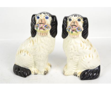 An opposing pair of Staffordshire type ceramic spaniels holding baskets of flowers, height 20cm. CONDITION REPORT: One extens