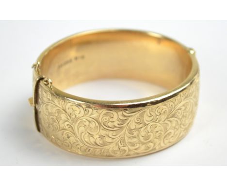 A 9ct yellow gold snap bangle overall engraved with foliate scroll decoration, oval 6 x 5.5cm, 31g (safety chain af).