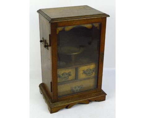 An early 20th century oak smoker's cabinet, the single glazed door enclosing tobacco jar stand above two short and one full l