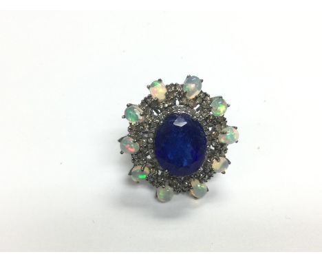 A large vintage style cocktail ring in white metal set with an oval tanzanite surrounded by oval cabochon opals and R/C diamo
