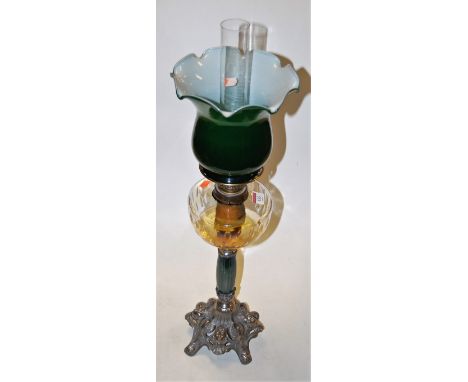 An Art Nouveau style oil lamp having green frilled glass shade above a clear glass reservoir on pierced pewter scrolling base