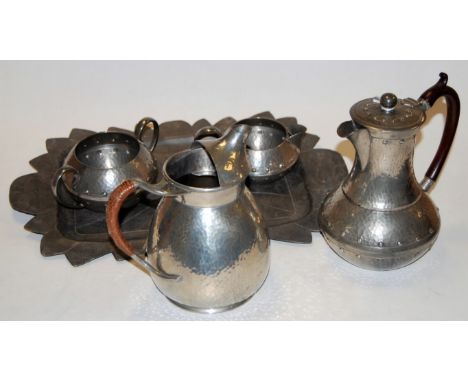 An Arts & Crafts spot hammered pewter three piece tea service together with an associated hot water jug on further associated