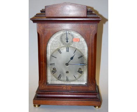 An early 20th century mahogany satinwood and pearwood inlaid cased bracket clock having a silvered arched dial with Roman num