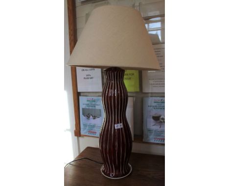 A red glazed ribbed pottery table lamp together with plain shade