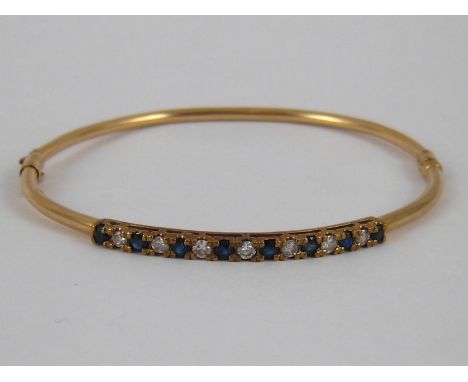 A yellow metal (tests 9 carat gold) sapphire and diamond bangle, internal width approx. 5.5cm, 5.4 gms.