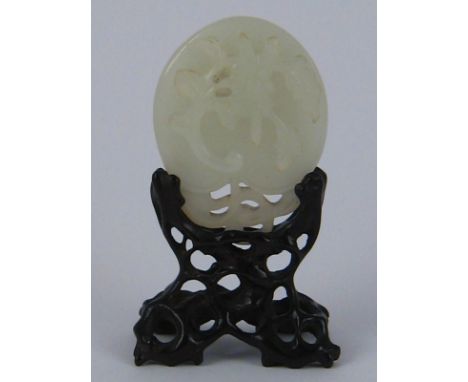 A Chinese jade ornament carved as a leaf and flower in an intricately carved hardwood stand. Ht.8cm. 