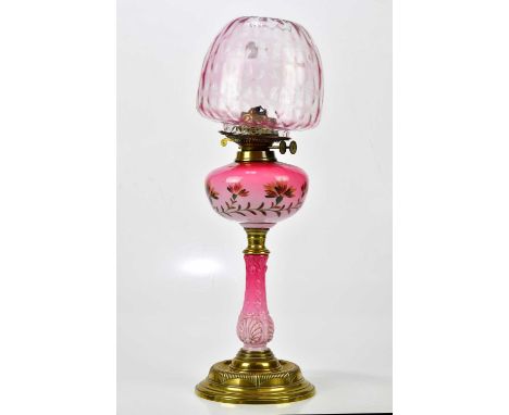 A late Victorian cranberry and milk glass oil lamp with cranberry tinted shade, the reservoir painted with floral sprays on a