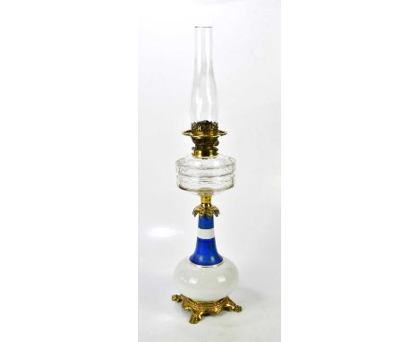 A Victorian milk glass oil lamp with gilt metal mounts and clear glass reservoir, raised on paw feet, height 74cm.