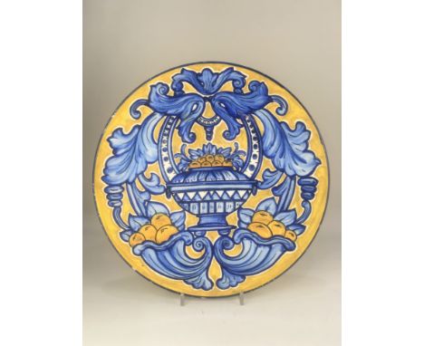 A Continental maiolica style wall plate, decorated with fruit filled cornucopia and vase, in yellow and blue on white ground,