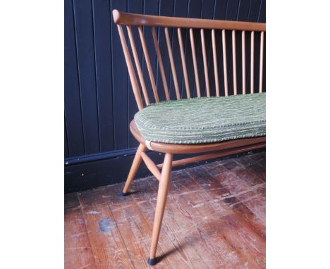 An Ercol love seat, the spindle back with cowhorn top rail, the solid seat with chamfered and wavy edge front, having a cushi