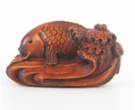 A carved boxwood netsuke in the form of a fish on a wave, signed, 5cm long. 