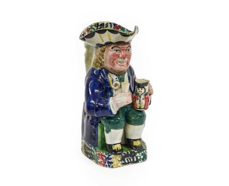 A Yorkshire Prattware Toby Jug, circa 1810, of traditional form with caryatid handle and ruddy face, the seated figure holdin