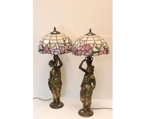 A pair of cast metal lamp bases in the form of classical women, with Tiffany style shades, approx 75cm tall to top of shade.