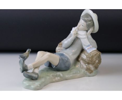A Lladro figure of a boy at rest with a bird on his foot singing. 