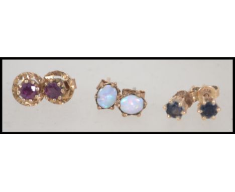 Three pairs of 9ct gold stud earrings individually set with opal, red stone and dark stone. Total weight 3 g.