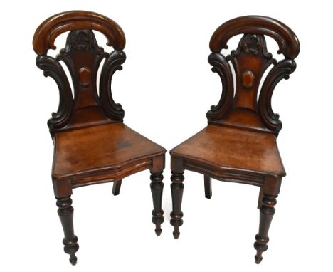 A pair of Victorian mahogany hall chairs with carved backs and shaped seats on turned and tapered front supports (one af).Add