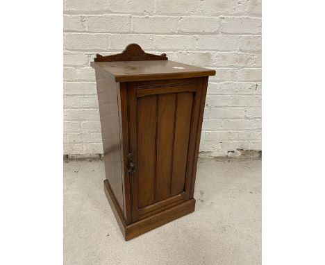 An Edwardian walnut bedside cabinet with moulded gallery back the panelled door before single shelf to interior on plinth bas