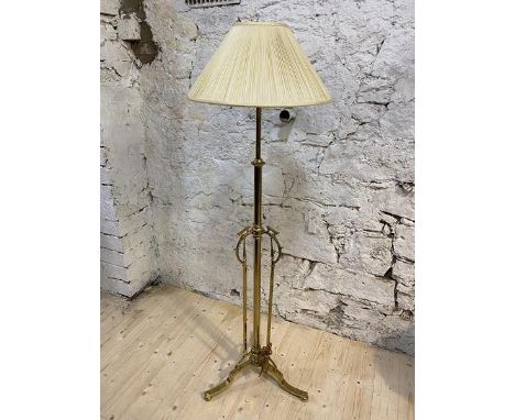 A brass standard lamp with adjustable stem, having three supports with C scrolls, on tripod support, (180cm to top of shade, 