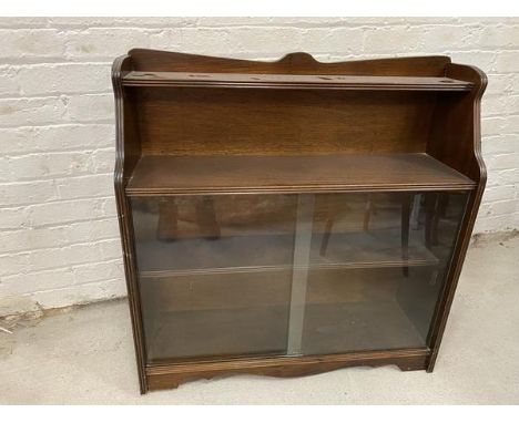 A waterfall bookcase with moulded top above single shelf, base with two sliding glass doors before single shelf to interior, 