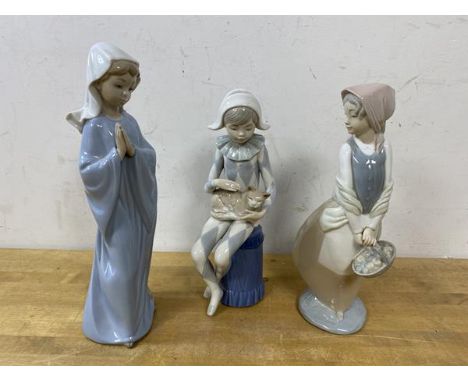 A Spanish Nao figure of a harlequin seated holding cat, (23cm high), and a young girl praying and a girl carrying a basket (3