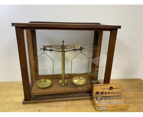 A vintage set of balance scales in display case marked Sold by A H Baird Edinburgh, and a box of weights, one weight lacking,