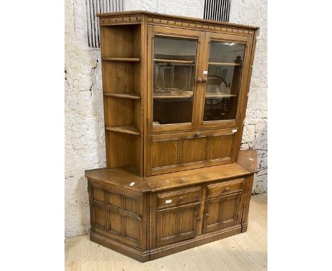 An Ercol elm dresser with two glazed doors with plate rails to interior over fall front door, having glass shelves and storag