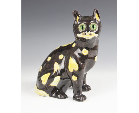 A Mosanic pottery model of a seated cat, decorated with naïve hearts and circles against a black ground, green glass eyes, 21