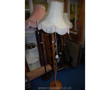 A wooden standard lamp with a fringed, cream and pink shade.