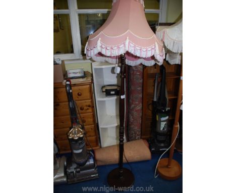 A wooden standard lamp with a fringed, cream and pink shade.