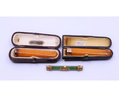 Two butterscotch amber gold mounted cheroot holders and a jade brooch&nbsp;