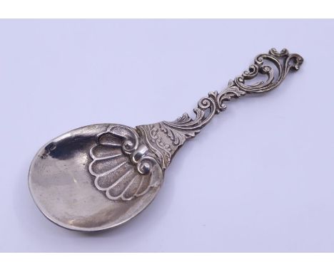 A continental white metal caddy spoon with pierced leafage scroll handle and circular bowl with scallop shell detail. bowl st