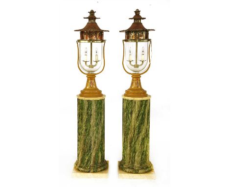 A pair of lamps and columns, 20th century, each with a copper lantern canopy over an inverted glass lantern, with two lights 