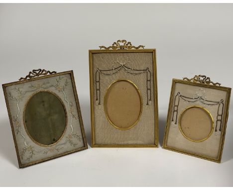 Three Edwardian gilt-metal and silk needlework photograph frames, of similar design, each with ribbon-tied surmount, the fram