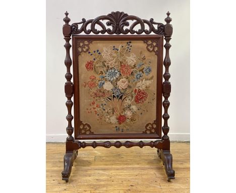 A large mid-Victorian mahogany needlework fire screen, the rectangular panel worked in polychrome threads with a cornucopia o