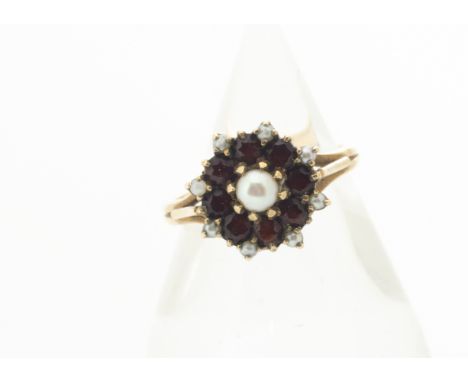A contemporary garnet and pearl yellow metal cluster ring, the central claw set pearl surrounded by circular cut garnets and 