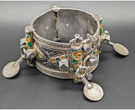 A North African Berber silver tribal bangle with yellow, green and black enameling, mounted with coins depicting Arabic, 208g