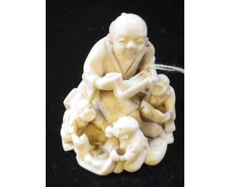 A JAPANESE IVORY NETSUKE, in the form of a seated figure, surrounded by children