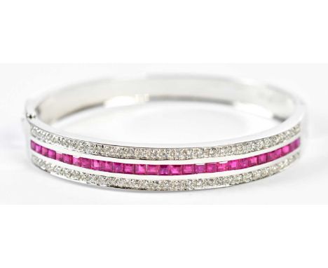 An 18ct white gold diamond and ruby hinged oval bangle set with central row of square cut rubies flanked by twin rows of roun