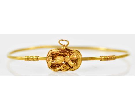 An unusual yellow metal bangle modelled after the antique with stylised flowerhead panel, approx 9.5g.