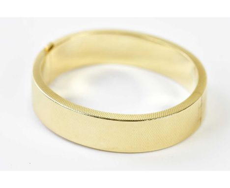 A yellow metal oval hinged snap bangle with engraved detail throughout, the tongue stamped ‘585’, internal width 60mm, approx