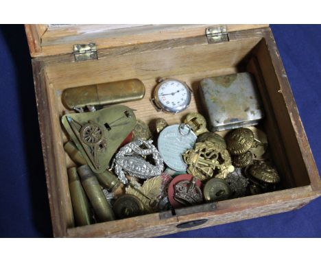 A vintage box containing military badges, buttons and a silver cased military style wristwatch