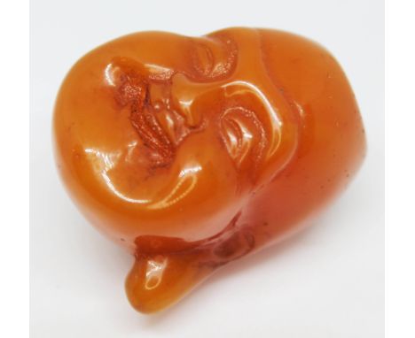 A pressed amber netsuke formed as a buddha's head, length 40mm, gross wt. 20.3g.  