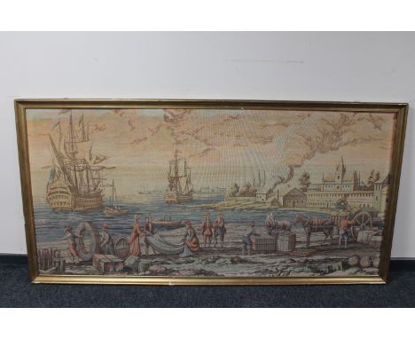 A gilt framed tapestry of boats landing in a harbour 