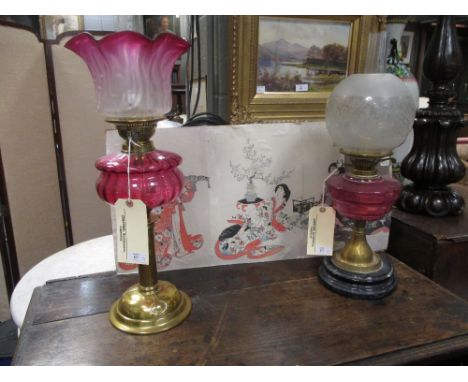 An Art Nouveau style brass oil lamp with a cranberry glass reservoir and graduated shade, 55cm high, together with another oi