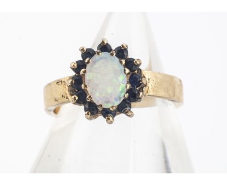 A 14k marked opal and sapphire cluster ring, oval cabochon precious opal in claw setting surrounded by a bezel of sapphires, 