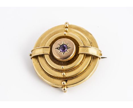 A 19th century amethyst yellow metal target brooch,  the central stone in gypsy setting beaded and banded decoration, open wo